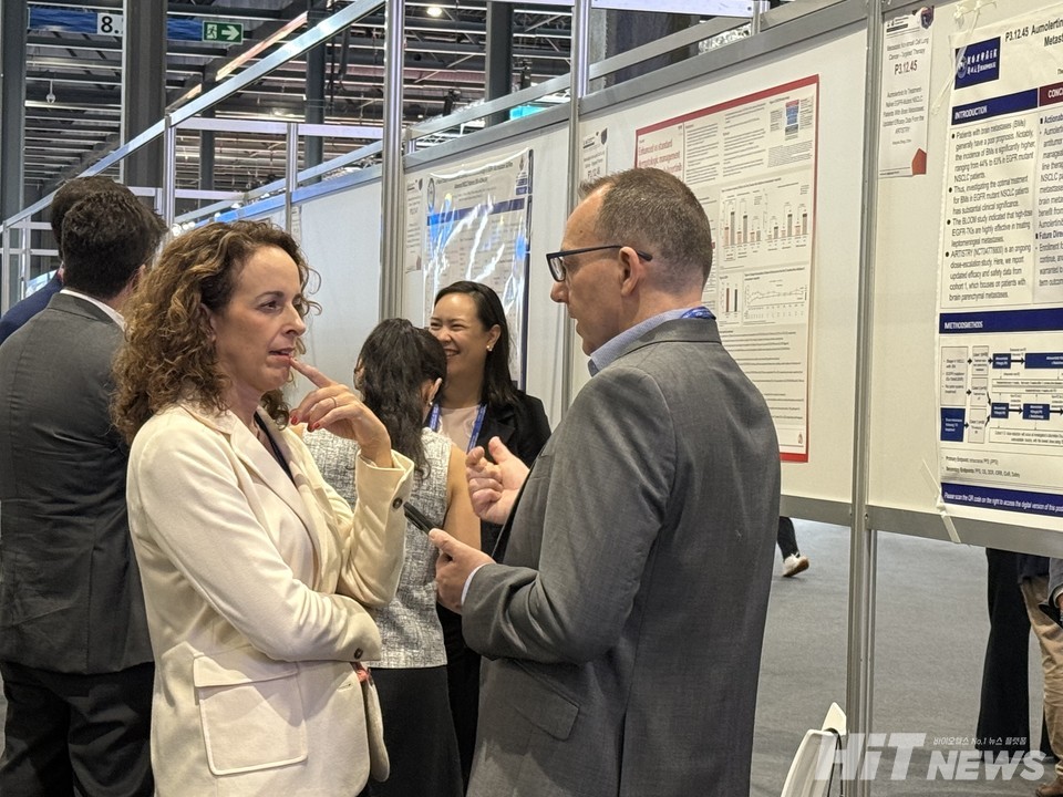 참가자들이 리브리반트+렉라자 피부 치료 포스터 앞에서 대화를 나누고 있다.